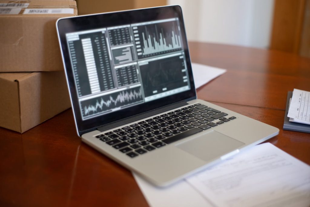 Laptop Displaying Charts Standing on the Table next to Cardboard Boxes